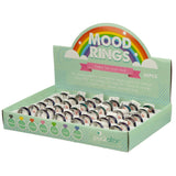 Angled view of a light green point-of-sale display box containing 36 mood rings. The header features a rainbow design and MOOD RINGS text, with explanatory text about the rings containing thermoactive liquid crystal that changes colour to indicate emotional state. The front of the box displays various moods such as 'Anxious', 'Stressed', and 'Relaxed' with colourful diamond icons. Each ring has a silver-coloured band and a dark, iridescent top.
