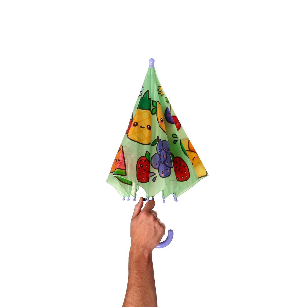 A hand holds open a kids' umbrella with a colourful cartoon fruit pattern, revealing the light green canopy, purple handle, and matching rib tips.
