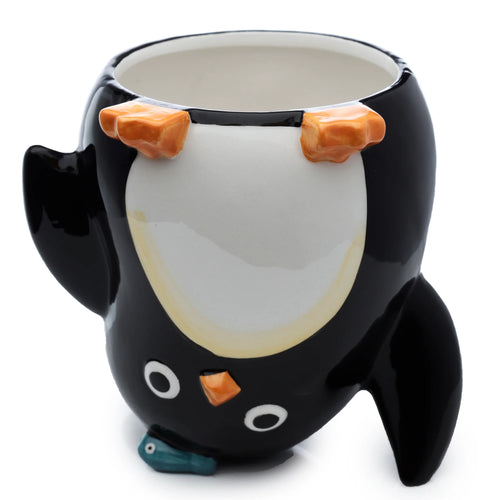 Angled view of a black and white ceramic upside-down penguin mug, showing orange feet at the top, a white belly, and the penguin's face with an orange beak and small blue fish at the base.