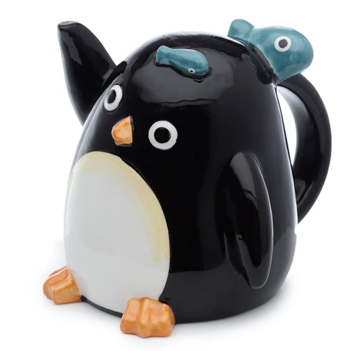 A glossy black ceramic penguin-shaped mug with a white belly, orange beak, and orange feet. Two small blue fish are on its head, and a black handle is visible on the right.