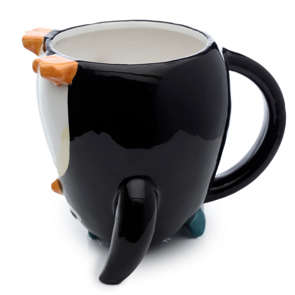 Angled view of a glossy black and white ceramic mug shaped like an upside-down penguin, featuring orange feet on the rim, an orange beak, a black handle, and teal feet at the base, showcasing its white interior.