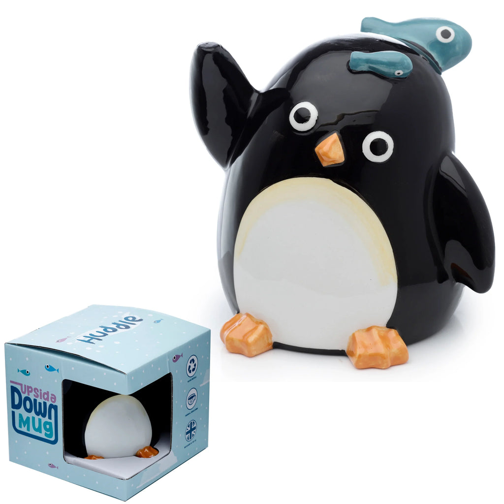 Angled view of a glossy black and white ceramic penguin mug, featuring an orange beak, orange feet, and two blue fish on its head, placed next to its light blue product packaging box.