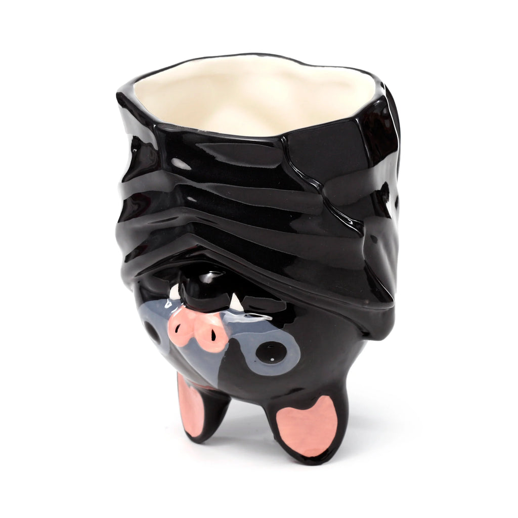 Angled front view of a glossy black ceramic novelty upside down bat mug, featuring pink feet, a pink nose, white fangs, and grey facial details, with a cream-coloured interior visible.