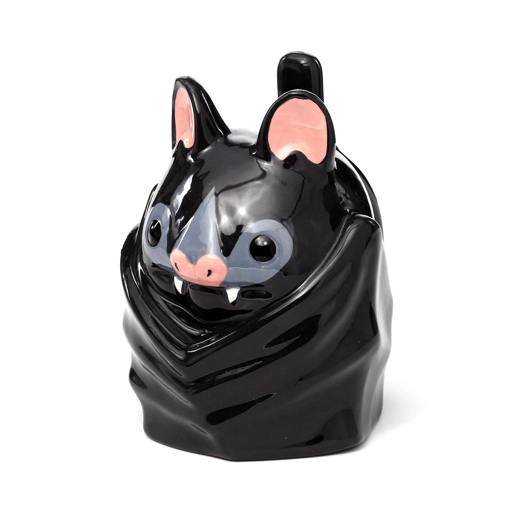 Angled front view of a black ceramic novelty upside down bat mug, featuring pink ears, a pink nose, grey eye detailing, and white fangs.