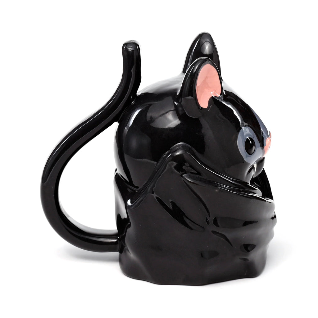Angled view of a glossy black ceramic upside down bat mug, featuring pink inner ears, a pink nose, and grey eyes. The bat's tail forms the curved handle.