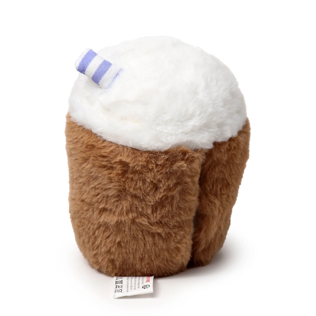 Angled view of a microwavable plush bubble tea heat pack, with a fluffy brown body, a soft white topping, and a purple and white striped straw, showing a care label at the base.