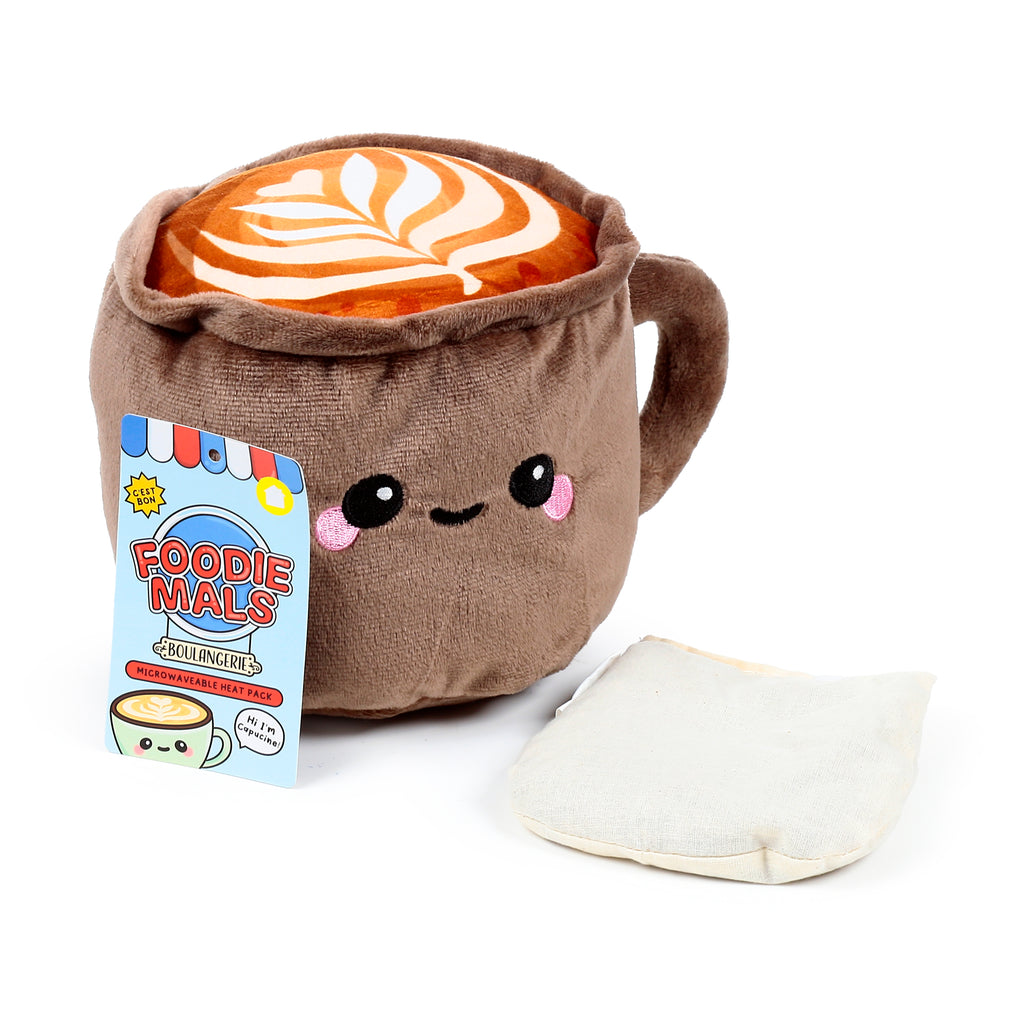 Front view of a brown plush cappuccino-shaped microwavable heat pack featuring an embroidered face and latte art, displayed with its detached cream fabric insert and a blue product tag.
