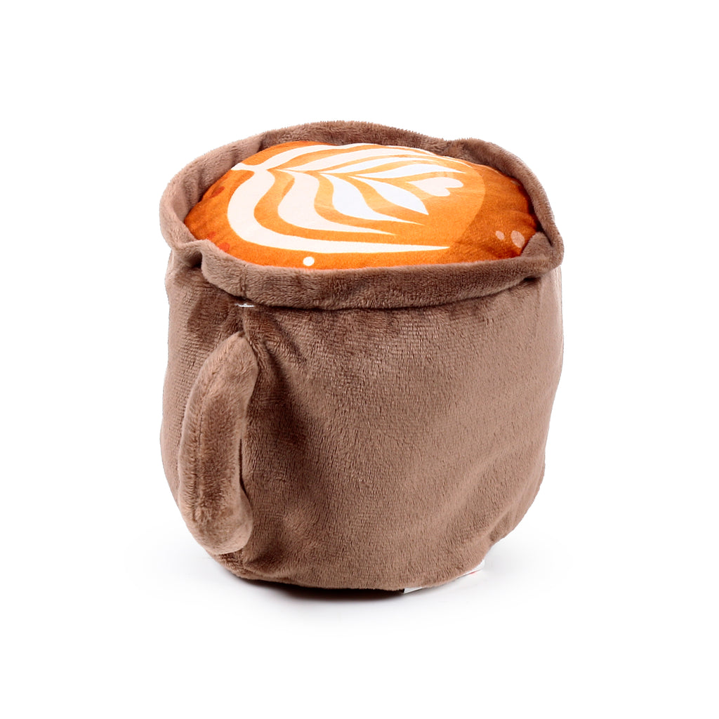 Angled view of a brown plush heat pack in the shape of a cappuccino mug, with a handle and white latte art on its orange top surface.