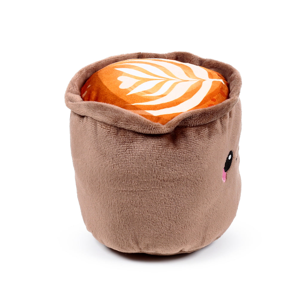 Microwavable plush heat pack shaped like a cappuccino cup, showing latte art and a cute embroidered face with an eye and pink tongue on the side.