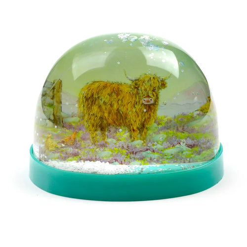 Glitter snow globe depicting a shaggy Highland Coo in a field of purple heather, with white glitter snow and a teal base.