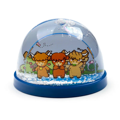 Angled view of a glitter snow globe depicting three cartoon Highland Coo cows in a pastoral scene with a dark blue base.