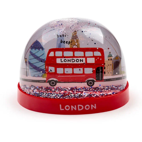 Glitter snow globe featuring a red double-decker London bus with iconic city landmarks like Big Ben and The Gherkin inside, set on a red base with 'LONDON' text. The globe contains red, white, and blue glitter.