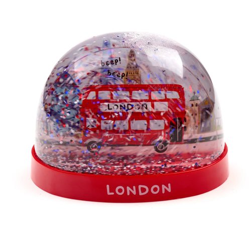 Angled view of a 7 cm tall London Bus glitter snow globe. Inside, a red double-decker bus with 'beep! beep!' text and Big Ben are surrounded by red, white, and blue glitter. The globe's red base features 'LONDON' in white capital letters.