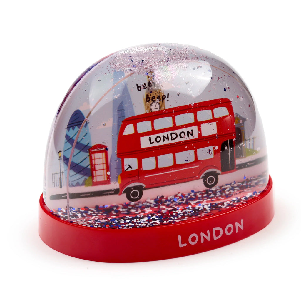 Angled view of a London glitter snow globe featuring a red double-decker bus, Big Ben, The Gherkin, and a red telephone box inside. The scene is surrounded by red, white, and blue glitter, and the globe sits on a red base displaying LONDON.