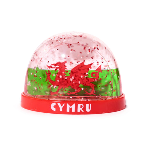 Front view of a Welsh dragon snow globe with red glitter. The clear dome shows a red dragon against a green background, set on a red base with 'CYMRU' in white text.
