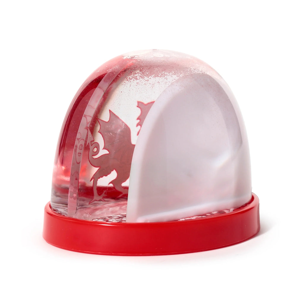 Angled view of a snow globe with a red base and clear dome. A red Welsh dragon silhouette is visible inside, surrounded by white 'snow' particles.