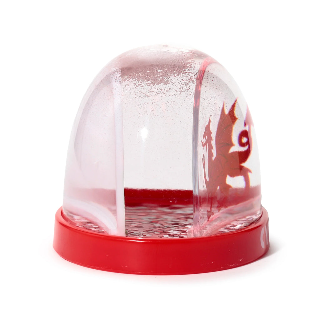 Angled view of a snow globe with a clear dome and red base, featuring a red Welsh dragon silhouette, red liquid, and red glitter.