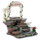 Angled view of a Fairy & Unicorn World figures display stand. It features tiered rock-effect platforms, an archway with 'FAIRY & UNICORN WORLD' text, green vine detailing, red flowers, and blue waterfall details.