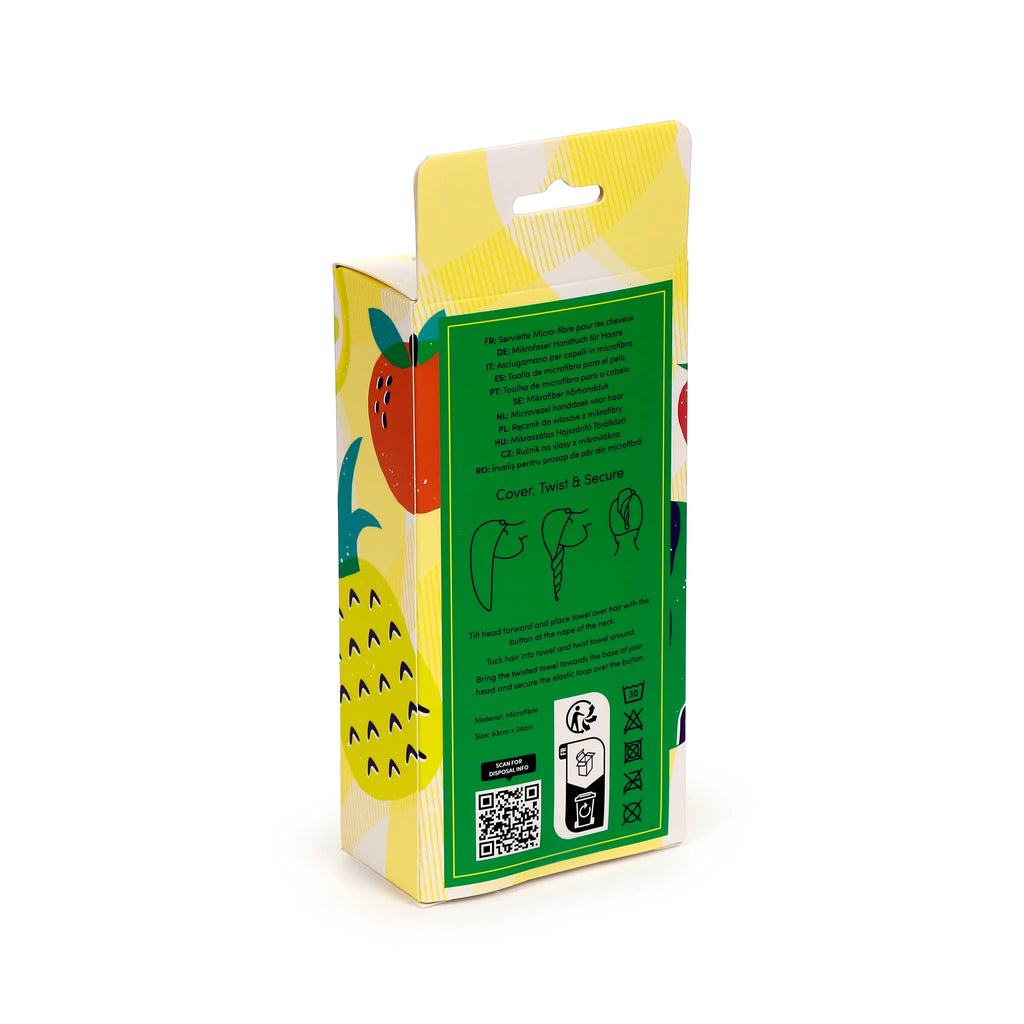 Angled view of a hair wrap towel's yellow and white plaid patterned cardboard packaging with a hanger slot. The packaging features red strawberry and partial pineapple illustrations, and a green information label displaying multi-language text, usage instructions, microfibre material, 63cm x 24cm size, and care symbols.