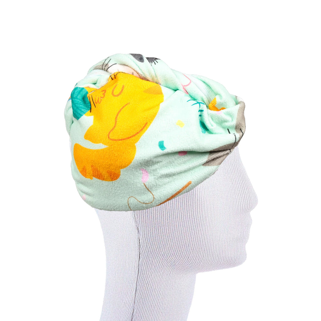 Side view of a mint green hair wrap towel featuring a cartoon cat pattern, including a prominent yellow cat face, on a white mannequin head.