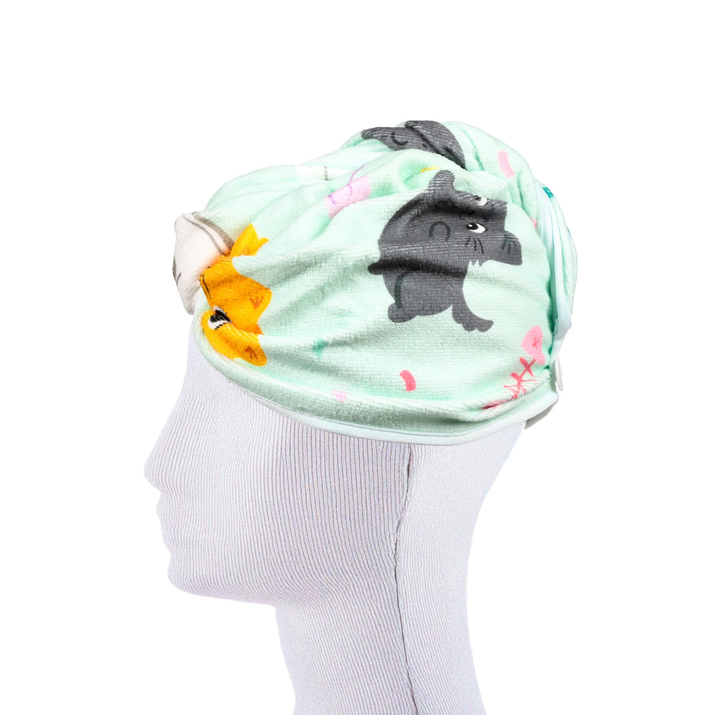 Side view of a mint green hair wrap towel featuring cartoon grey and orange cats, modelled on a white mannequin head.