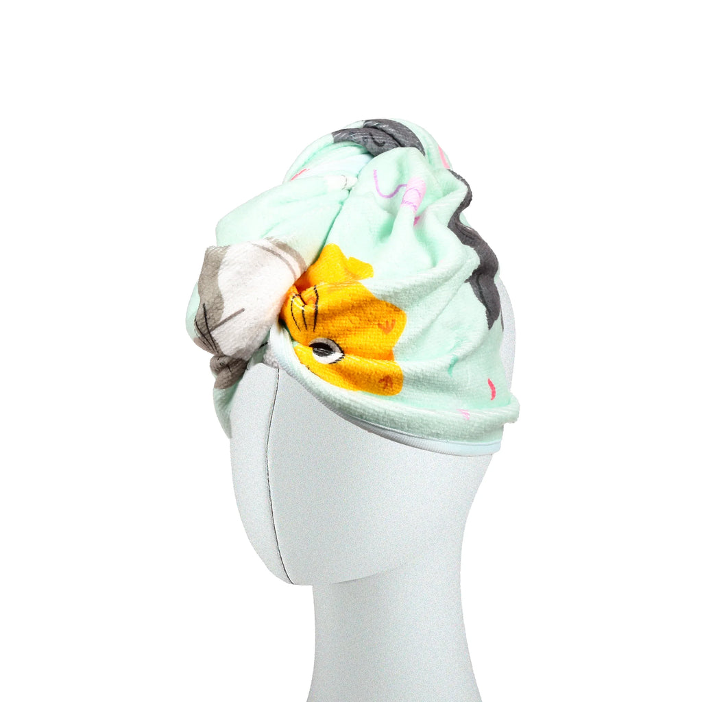 Angled view of a mint green hair wrap towel with a cartoon cat pattern, featuring a yellow cat face, on a white mannequin head.