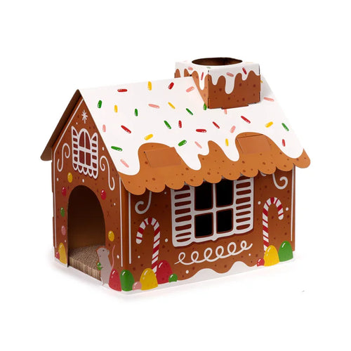 Angled view of a Christmas gingerbread house cardboard cat den playhouse, with white icing, colourful sprinkles, an arched entrance, a mouse graphic, and a visible scratching pad.