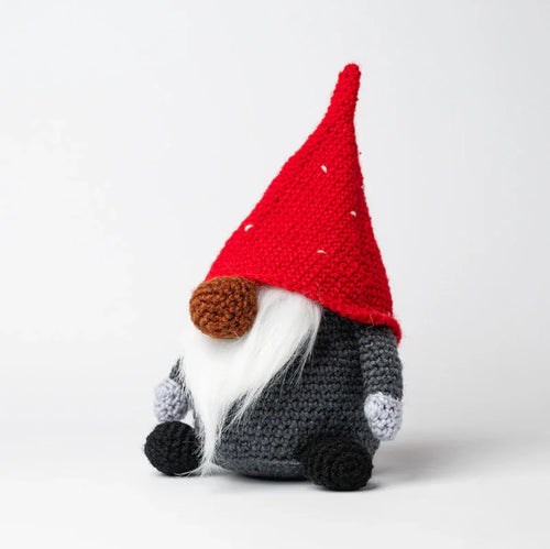 Angled front view of a crocheted Christmas gonk, featuring a red hat with white flecks, a white beard, brown nose, dark grey body, light grey cuffs, and black feet.