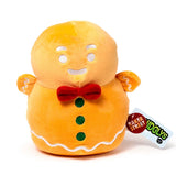 Front view of a Christmas gingerbread man plush toy. The orange plush toy features white embroidered eyes, smile, and icing detail, a red bow tie, and three green buttons. Product tags visible on the right read 'Baker Street' and 'Squidglys'.