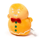 Front view of an orange gingerbread man plush toy, featuring a red bow tie, three green buttons, and white icing details.