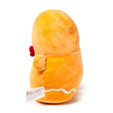 Angled view of a soft orange gingerbread man plush toy, showing its back, side, and white wavy icing detail near the base, with a fabric tag visible.