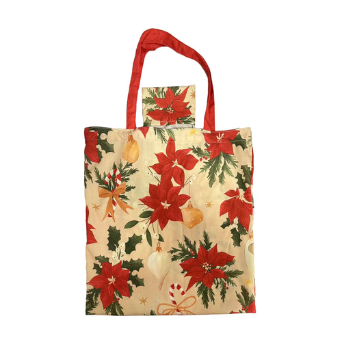 Front view of a cream reusable shopping tote bag with red handles, featuring a festive Christmas pattern of red poinsettia flowers, green holly, baubles, and candy canes, with a matching foldable pouch at the top.