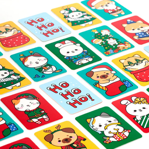 Angled view of numerous colourful Christmas memory cards for kids, featuring cartoon animals such as cats, bunnies, and dogs in festive outfits, alongside light blue cards with red 'HO HO HO!' text.