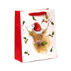 Angled view of a large white Christmas gift bag with red sides and red ribbon handles. The front features an illustration of a Highland Coo wearing a red Santa hat and holding green holly, surrounded by scattered holly leaves and red berries.