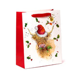 Angled view of a large white Christmas gift bag with red sides and red ribbon handles. The front features an illustration of a Highland Coo wearing a red Santa hat and holding green holly, surrounded by scattered holly leaves and red berries.