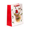 Angled view of a large Christmas gift bag featuring a Highland coo wearing a Santa hat, surrounded by holly and a robin on the white main panel, with red sides and ribbon handles.