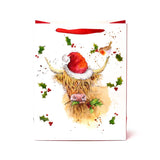 Front view of a large white Christmas gift bag with red ribbon handles, depicting a Highland coo wearing a red Santa hat, with a robin perched on its horn and scattered holly and berries.