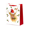 Front view of a large white gift bag with a red side panel and handles, featuring a Christmas illustration of a Highland Coo wearing a Santa hat, munching holly, with a robin and scattered holly leaves.