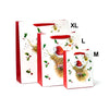 Angled view of a large white Christmas gift bag with red sides and handles. It is shown alongside medium and extra-large versions, each featuring a festive Highland Coo illustration wearing a red Santa hat, surrounded by holly and berries.