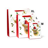 Angled view of a large white Christmas gift bag with red sides and handles. It is shown alongside medium and extra-large versions, each featuring a festive Highland Coo illustration wearing a red Santa hat, surrounded by holly and berries.