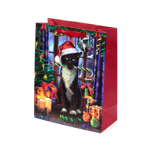 Angled view of a red Christmas gift bag with fabric handles. The front features an illustration of a black cat wearing a Santa hat, holding a striped candy cane, amidst a festive scene with a Christmas tree, wrapped gifts, and lit candles.