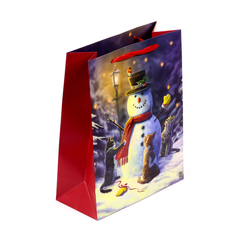 Large Christmas gift bag shown from an angled perspective, displaying a festive winter illustration on its main panel. The design features a snowman wearing a top hat and red scarf, surrounded by three 'Little Helpers' Christmas cats in a snowy scene with a lamppost. The bag has deep red side panels and red ribbon handles.