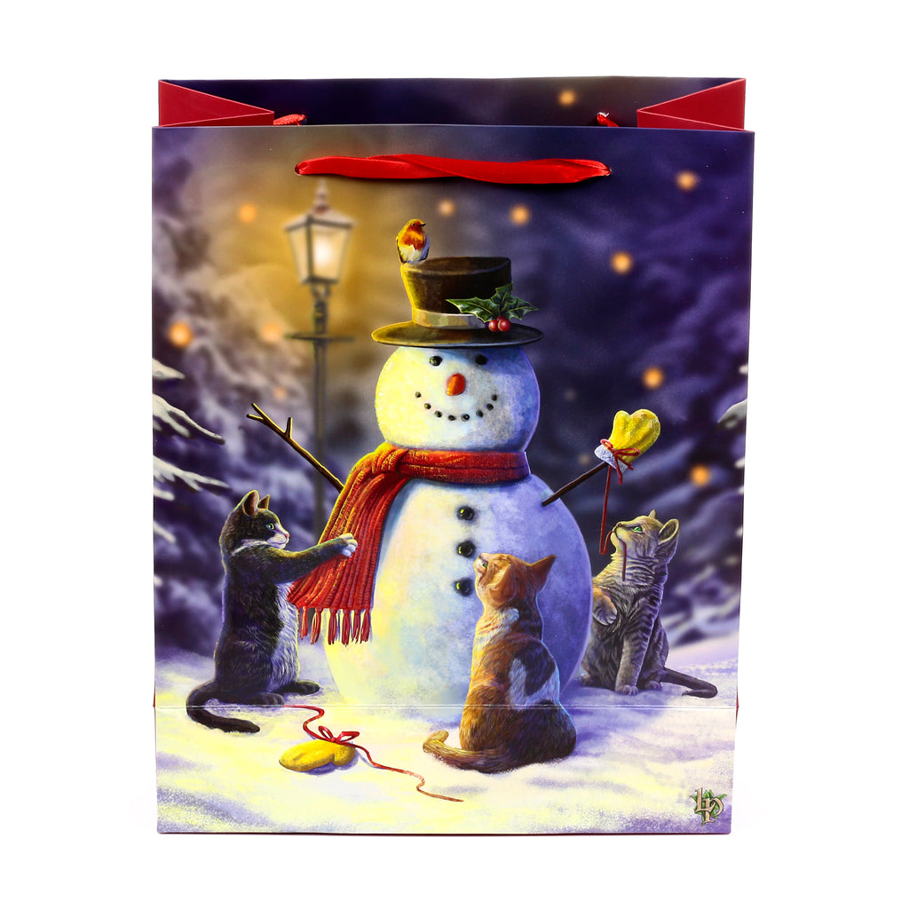 Front view of a Christmas gift bag with red ribbon handles, displaying a vibrant illustration of a snowman wearing a top hat and red scarf, surrounded by three cats playing in a snowy, lamplit winter night scene.