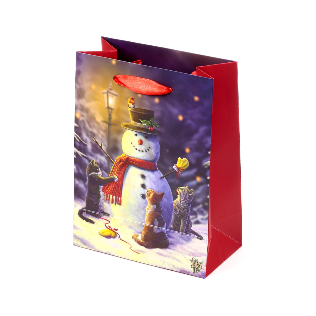 Angled view of a Christmas gift bag, showing a charming illustration of three cats surrounding a snowman in a snowy winter scene, complete with red ribbon handles and red side panels.