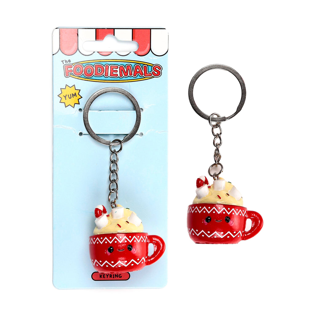 Front view of a hot chocolate cup keyring, featuring a red mug with a smiling face, white zig-zag patterns, and a topping of cream, marshmallows, sprinkles, and candy canes. The item is displayed both on its light blue packaging card and separately.