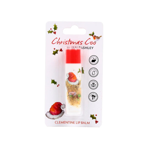 Front view of a Jan Pashley Christmas Highland Coo stick lip balm in clear and white card blister packaging. The packaging features a Highland cow illustration in a Santa hat holding holly, with holly sprigs and a robin bird. The lip balm has a red cap and a clear tube displaying the cow design. Text highlights 'Christmas Coo' and 'CLEMENTINE LIP BALM', with cruelty-free, moisturising, vegan, and palm oil free icons.