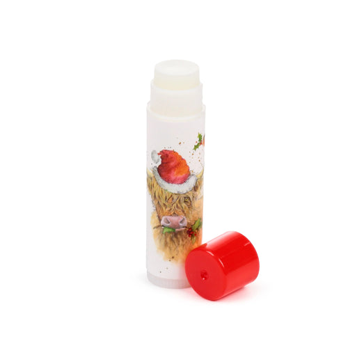 Stick lip balm with a Christmas Highland Coo design on a white tube, showing the coo wearing a red Santa hat and holding holly. The white balm stick is exposed, with the detached red cap lying beside it.