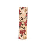 Paper stick lip balm standing upright, adorned with a Christmas botanical pattern of red poinsettias, green holly, and gold baubles on a natural-coloured background.
