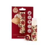A red display card featuring Christmas bauble illustrations and sustainability icons, holding a paper stick lip balm. Beside it, an open matching lip balm tube reveals the white balm and its separate lid. All items feature a festive red poinsettia and green holly pattern.