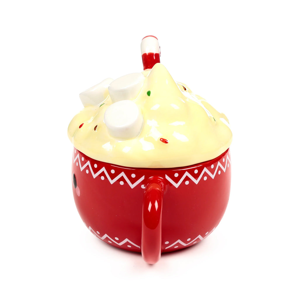 Angled view of a red ceramic lidded mug with a white zig-zag pattern, showing its red handle and cream-coloured lid decorated with white marshmallows, sprinkles, and a red and white stick.